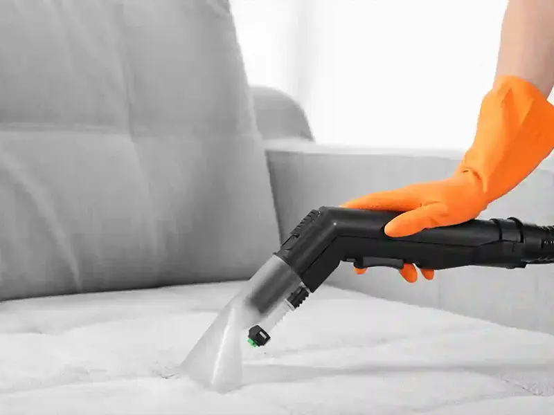 Pranie kanap w Jastrzębiu-Zdroju - ręka w pomarańczowej rękawiczce z końcówką maszyny czyszczącej kanapę